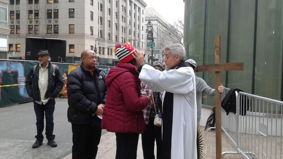 Man giving blessing in front of wooden cross on sidewalk
