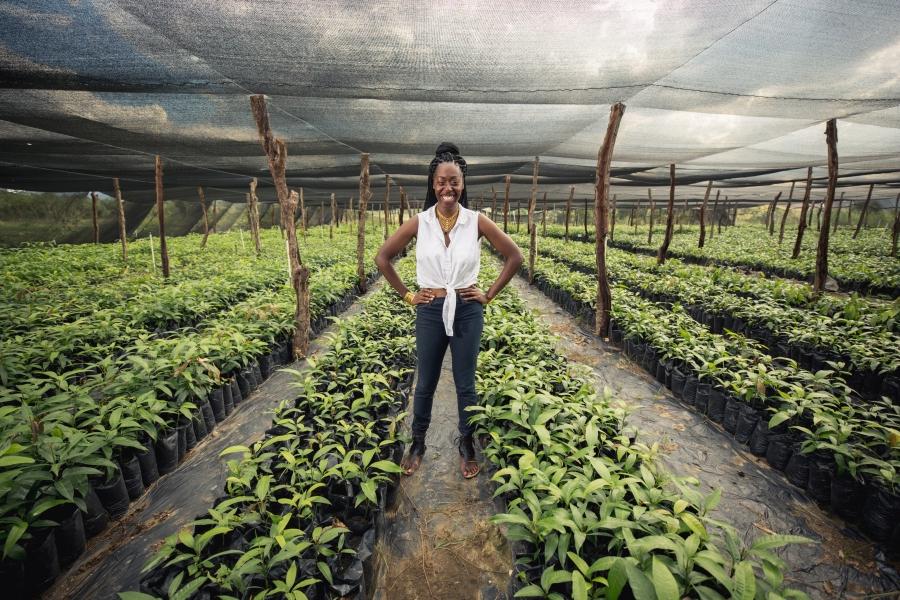 Woman stands in middle of rows of plants, greenhouse, smiling with hands on hips