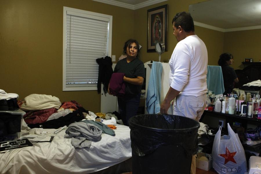 Man and woman looking at clothes and items strewn across a bed, being put in bags