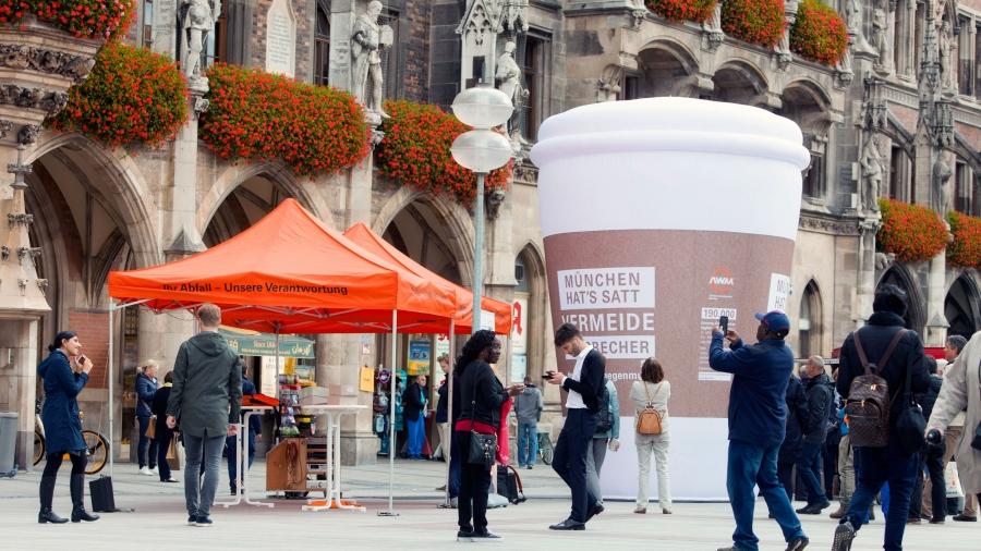 A giant inflatable coffee cup is set up in a public square. Behind it is an old Gothic church.