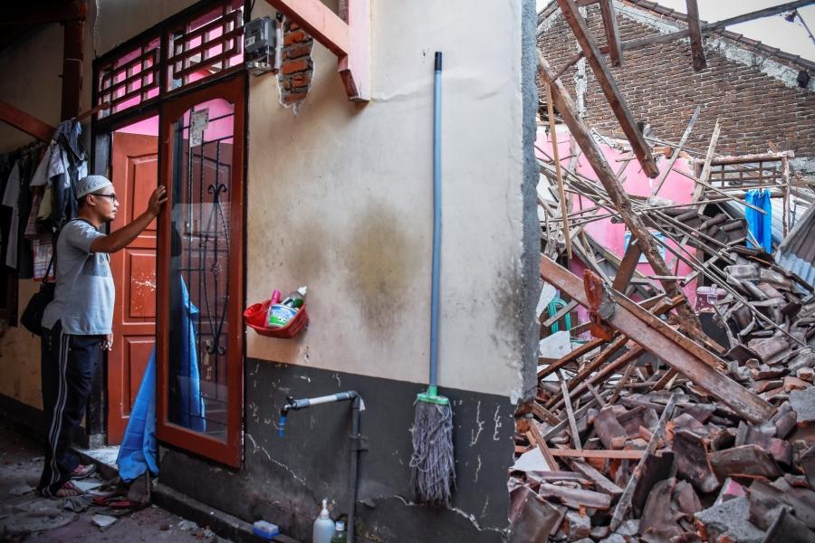 A man looks though a red doorway at debris from his partially collapsed home in Indonesia.