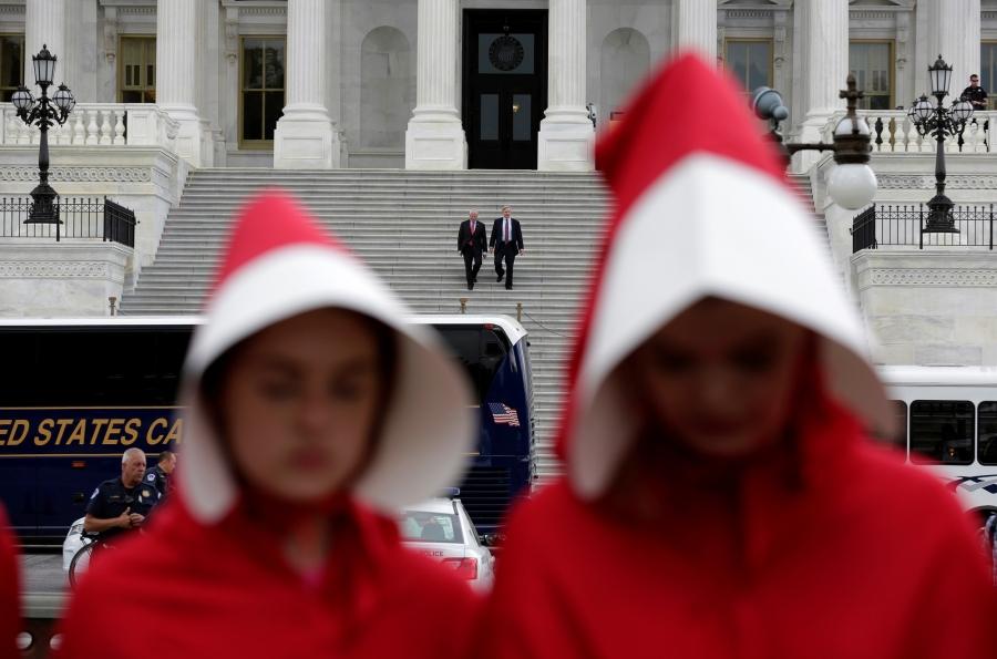 Senators Roger Wicker, a Republican from Mississippi, and John Hoeven, a Republican from North Dakota, walk down the steps of the Senate for a meeting at the White House as women dressed as handmaids demonstrate against the Senate healthcare bill at the U