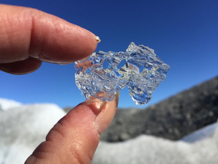 A clear piece of ice is held between a person's fingertips