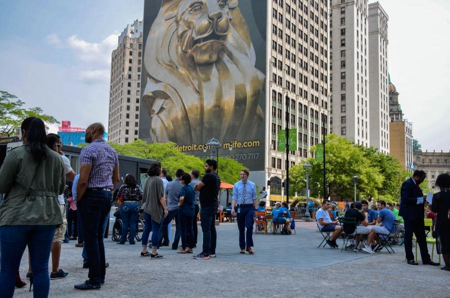 People are shown sitting at outdoor tables and standing in line for a food truck in downtown Detroit.