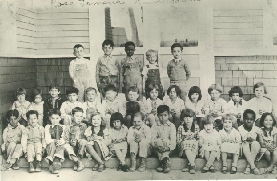 black and white photo of classroom, three rows of young children in shorts