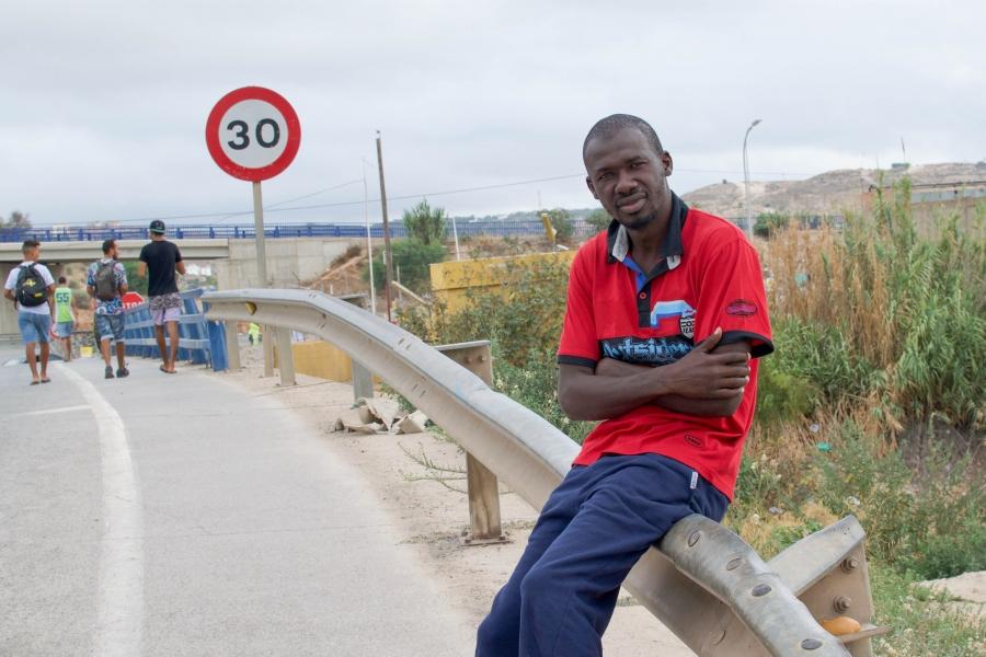 A migrant from Guinea sits on a railing outside outside of a detention center in Melillla, Spain