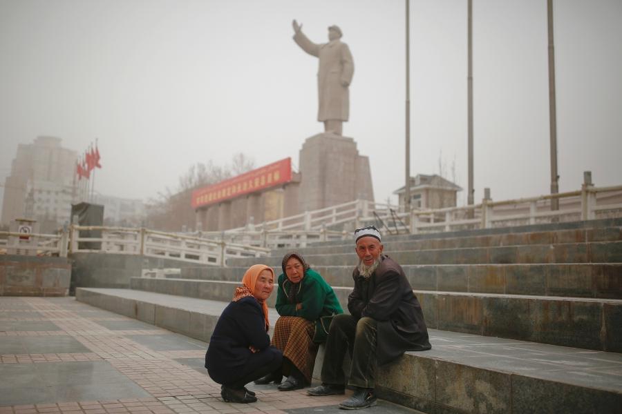 Ethnic Uighurs sit near a statue of China's late Chairman Mao Zedong in Kashgar.