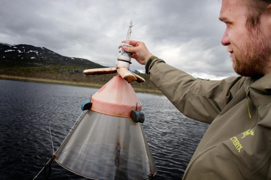 A man holds a piece of scientific equipment over a lake