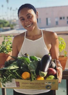 A young woman holds a box of veggies.