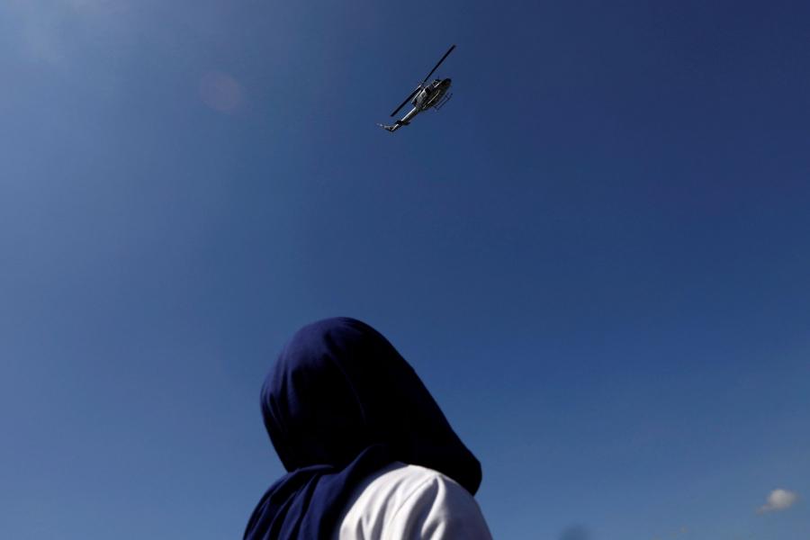 A Central American migrant is shown looking up as a military helicopter flies overhead.