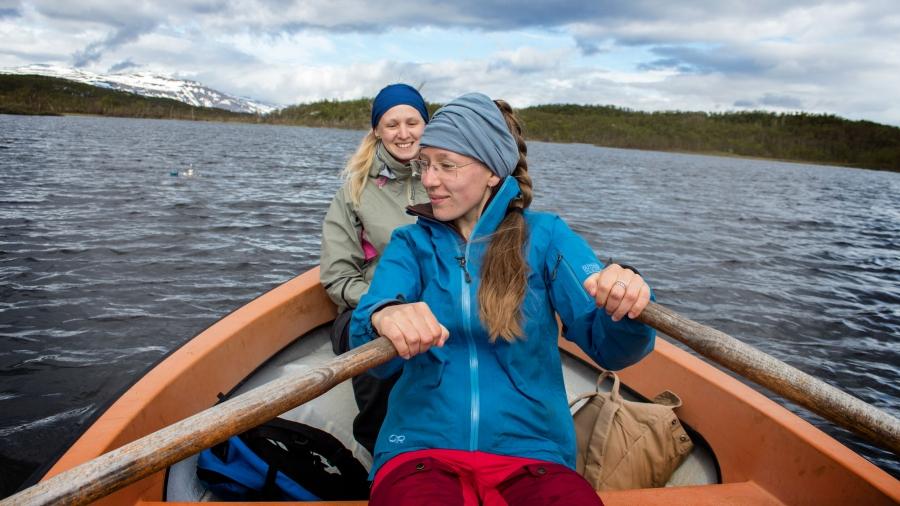 Two female student researchers in a row boat on a lake. 