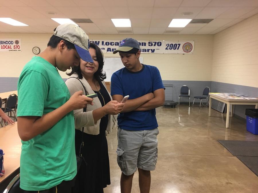 Woman stands with two young men leaning over her, looking at phone
