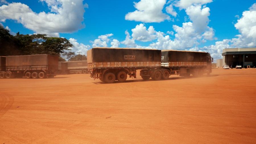 Big tractor trailer trucks kick up red dust as they pull toward building.