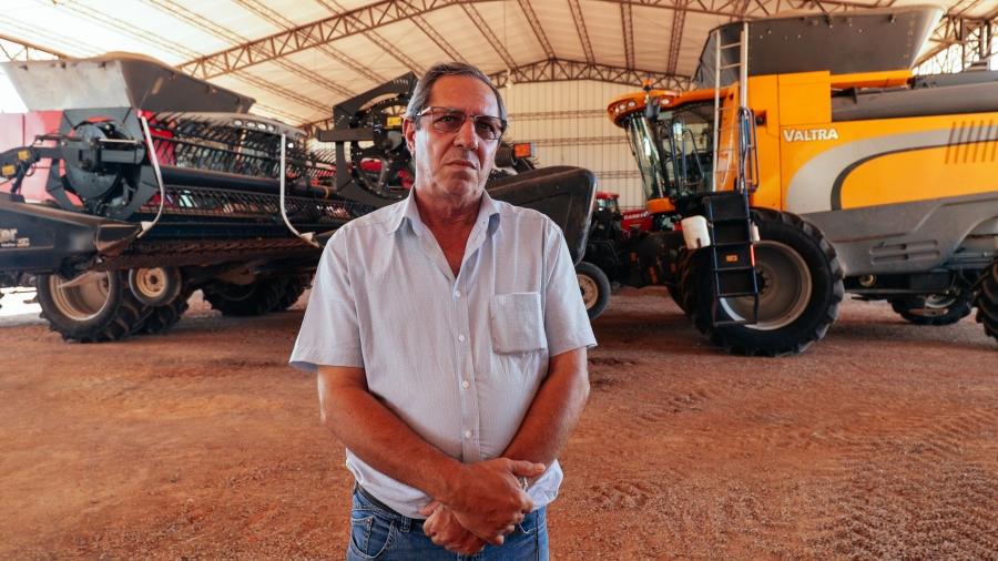 A man poses in front of heavy farm machinery.