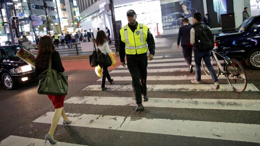 Antonio Nathaniel King, from the US, is shown wearing his security uniform walking across a street in Tokyo.