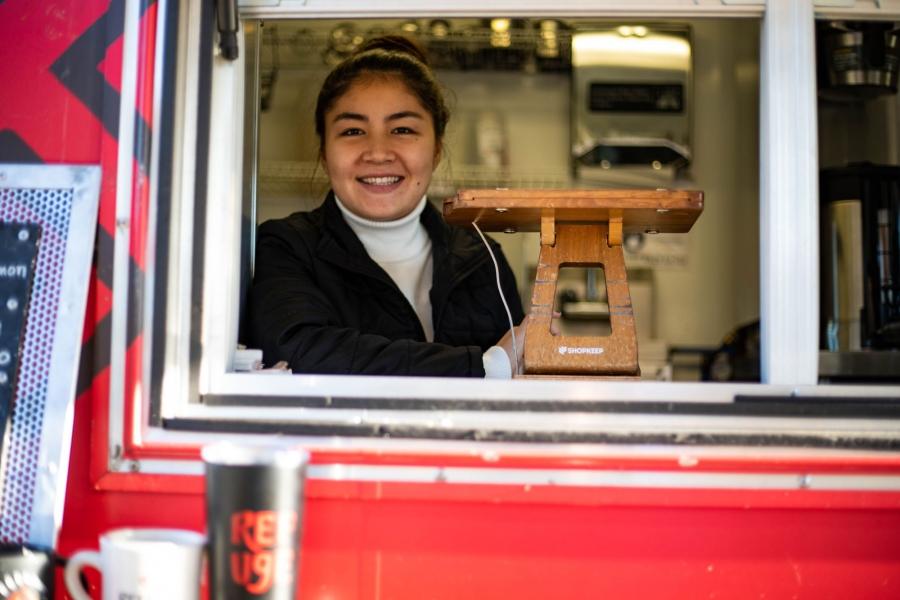 Afghan refugee and Refuge Coffee Co. employee Somayyah Maqsudi is shown smiling in the window of the coffee truck.