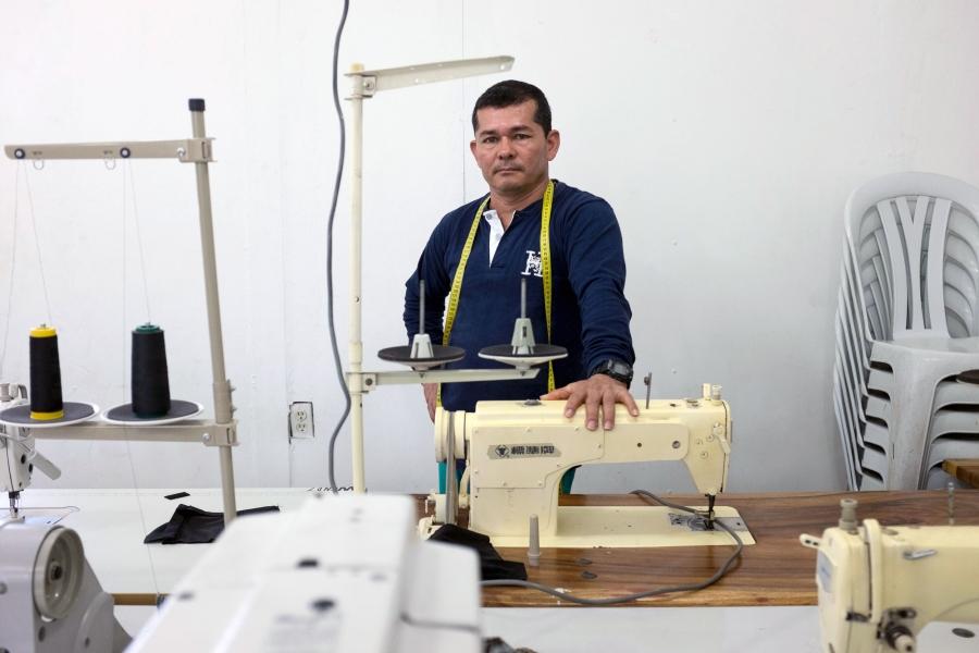 A man poses next to a sewing machine.