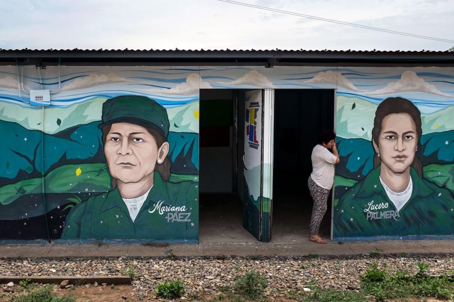 A woman leans in the doorway of a building with images of FARC leaders painted on the outside.