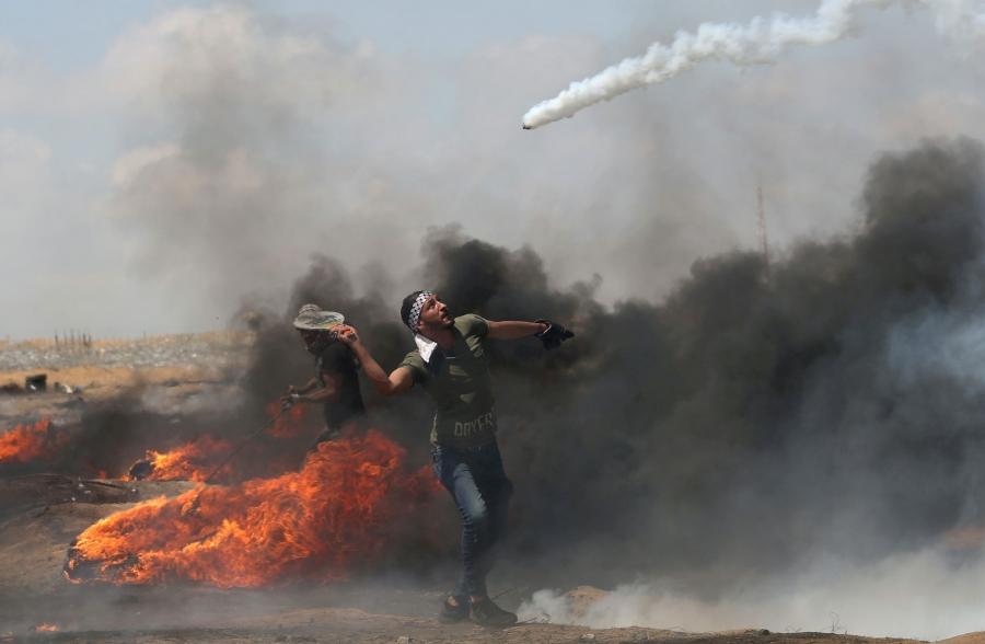 A man uses a racket to hit at a tear gas canister as it is launched through the air.