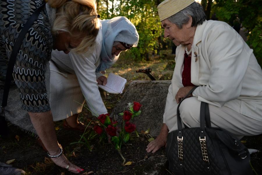 Three women stand around grave, pressing hands into soil