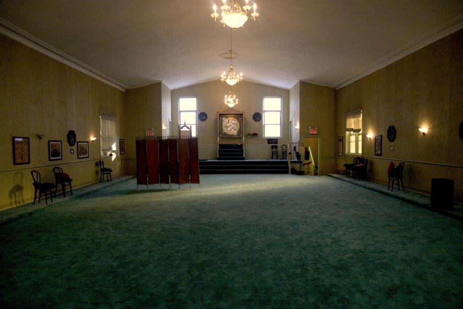 Main room of a mosque, with green carpet and a platform at front