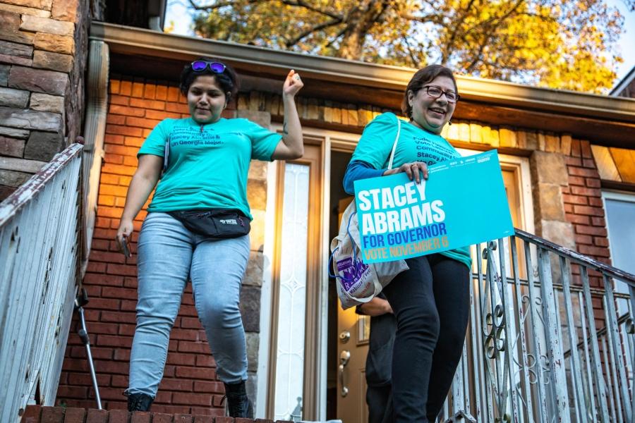 Gina Perez and her colleague wearing light blue t-shirts supporting Democrat Stacey Abrams, walk door stairs.