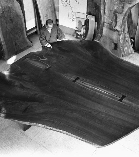 George Nakashima examines his third “peace altar.” It’s a table constructed with two giant cuts of black walnut attached together with butterfly joints. 