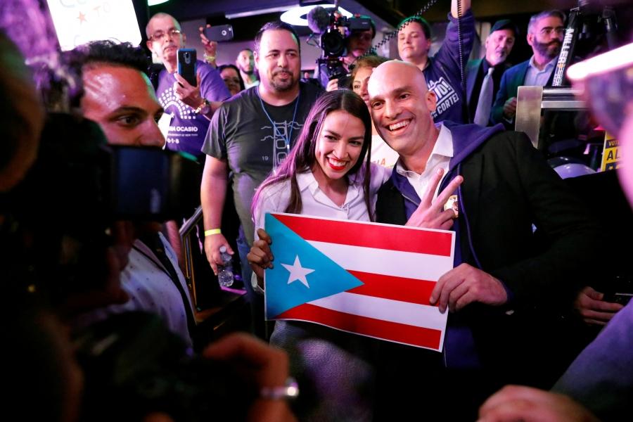 Representative-elect Alexandria Ocasio-Cortez holds a Puerto Rico flag and smiles 