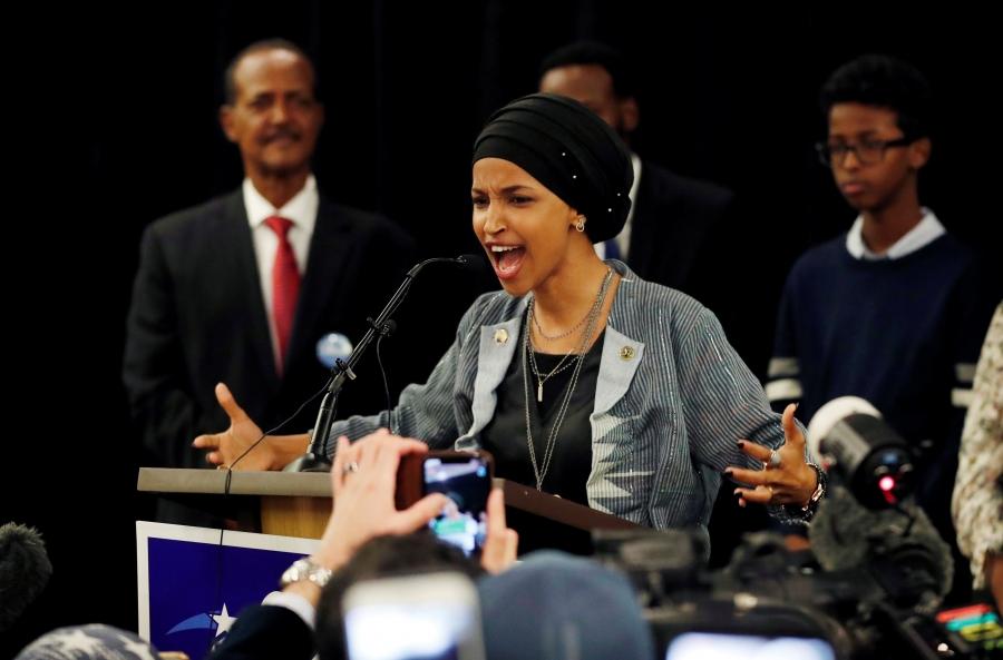 Ilhan Omar speaks at a podium with her arms held out 