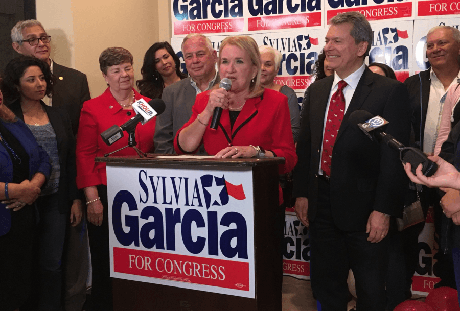 Sylvia Garcia speaks at a podium dressed in red in this photo from her campaign's Facebook page