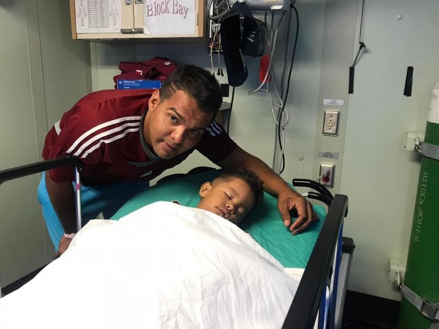 Eduardo Borges crouched over his son who is in a hospital gurney 