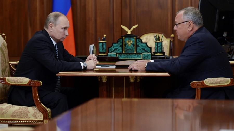 Two men sit with a desk in between them. On the left is Russian President Vladimir Putin.