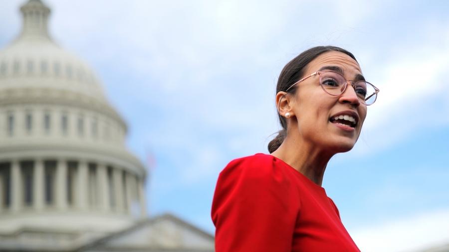 Alexandria Ocasio-Cortez wears a red dress with Capitol building in background. 