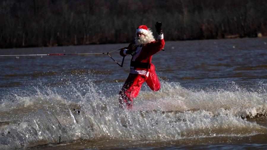 A man dressed up as Santa Claus waterskis on a river. 