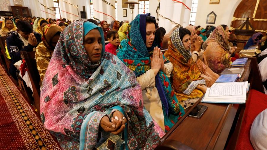 Women in colorful traditional dresses sit down and pray inside a church.