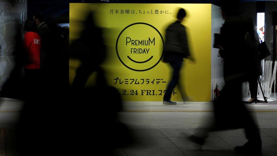 People walk by a bright yellow sign that says "premium day" in a smiley face.