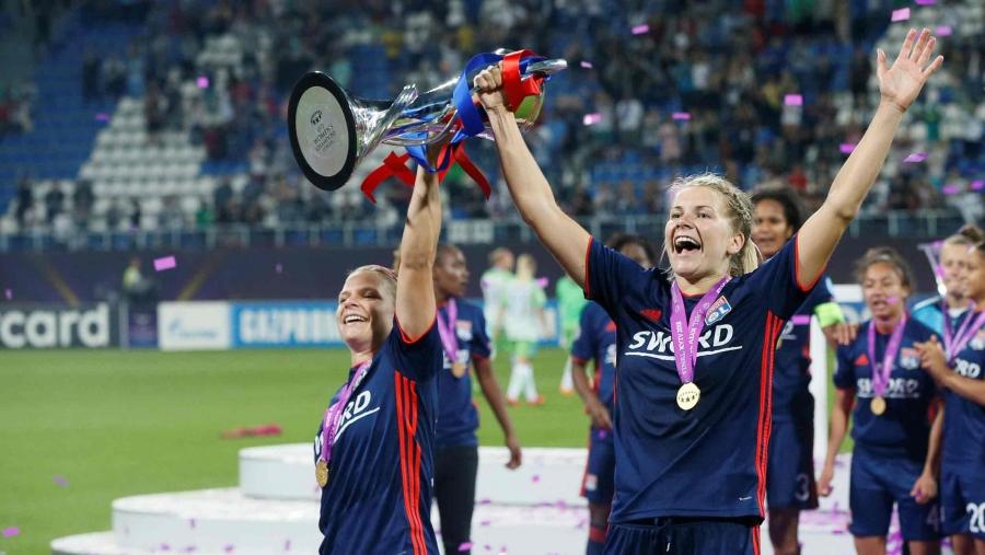 Ada Hegerberg celebrates on a soccer field, holding a trophy and a medal