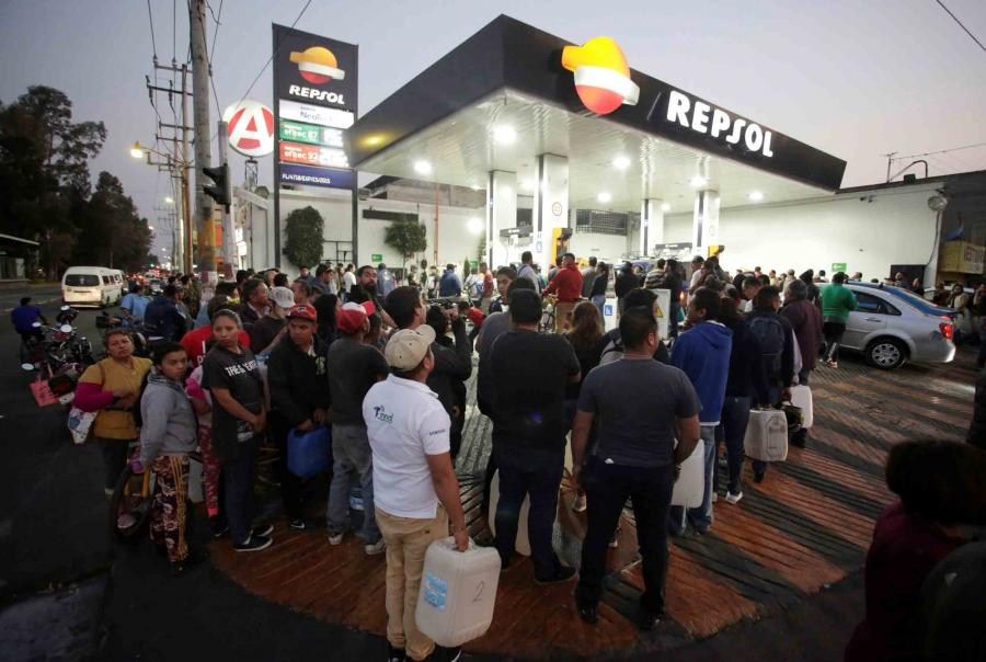 A crowd of people stand in line outside a gas station in Mexico with gas cans in their hands