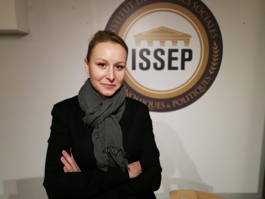 Marion Maréchal stands with her arms crossed in front of a ISSEP sign 