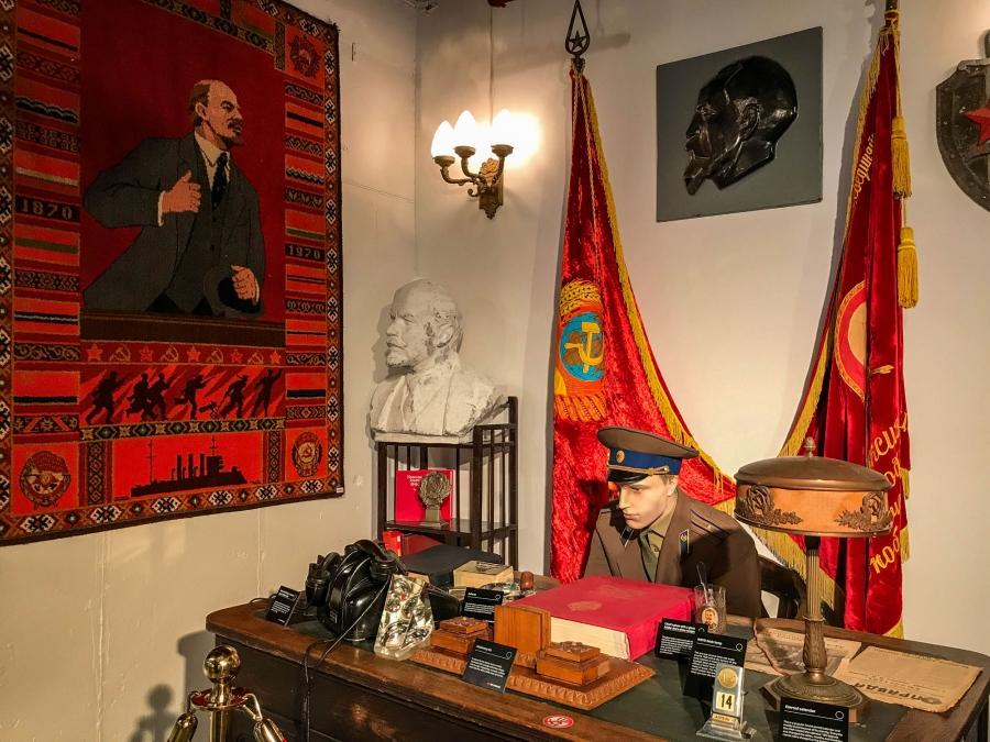 The museum’s recreation of a KGB office featuring a desktop calendar and a copy of the Communist newspaper, Pravda, with flags shown behind a uniformed mannequin. 