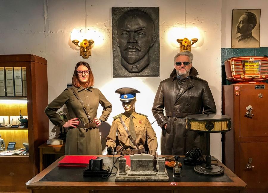 Father-daughter curators Julius Urbaitis and Agne Urbaityte pose behind a desk of a mannequin KGB duty officer wearing vintage military attire.