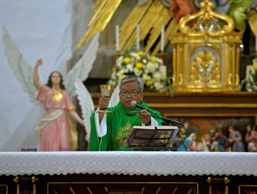Catholic priest Bobby Dela Cruz wears green robes and holds up a gold cup 
