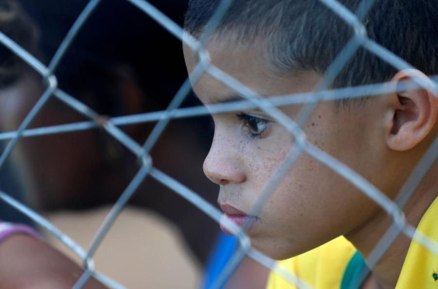 a closeup of a young boys face peering through a fence