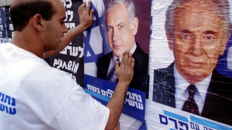 A man pastes a poster with the face of Netanayhu over the poster of Israel's then-prime minister. 