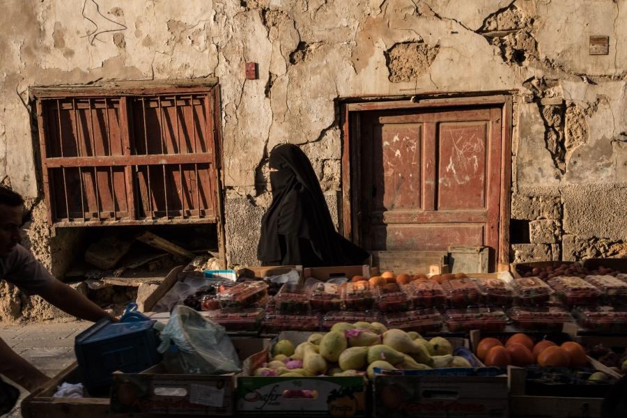 A woman passes a cart carrying produce in Al-Balad, Jeddah.