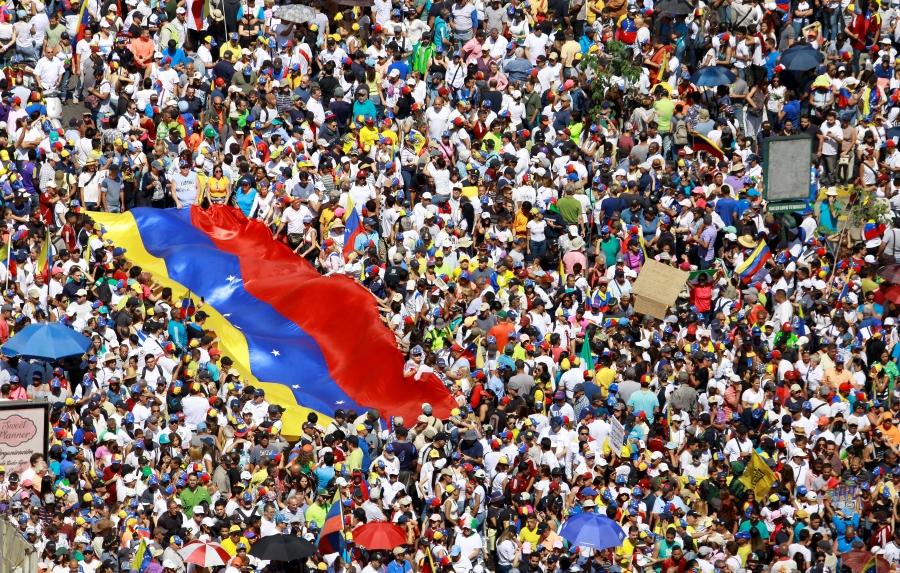 A massive crowd holds a large Venezuelan flag as they take part in a rally