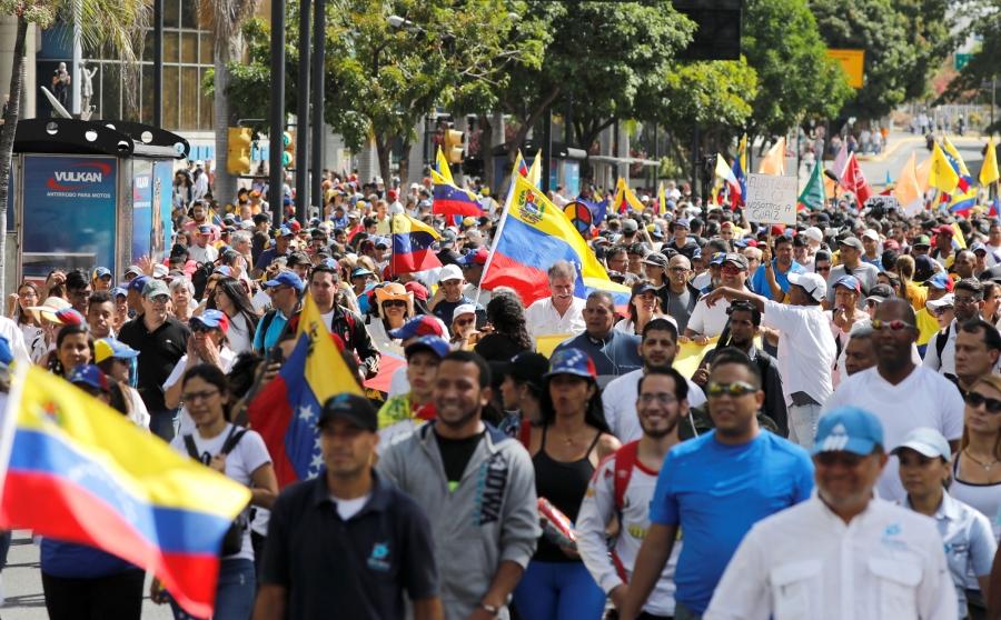 Opposition supporters are shown en masse in the street with placards and Venezuelan flags.
