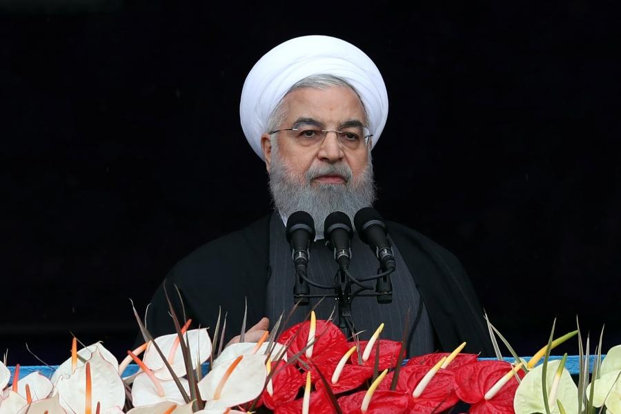 Iran's President Hassan Rouhani speaks behind a podium covered in red and white flowers 