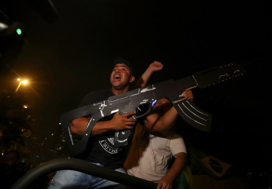 a man wearing a dark t-shirt holds a large cardboard gun 