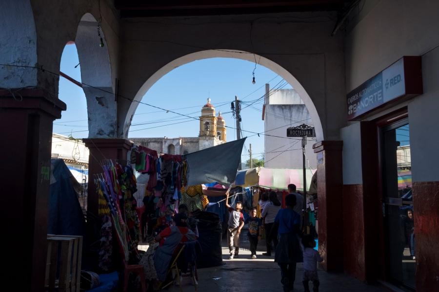 People are shown walking around at Tlaxiaco’s market, with the steeples of the Santa Maria de la Asunción church in the distance.